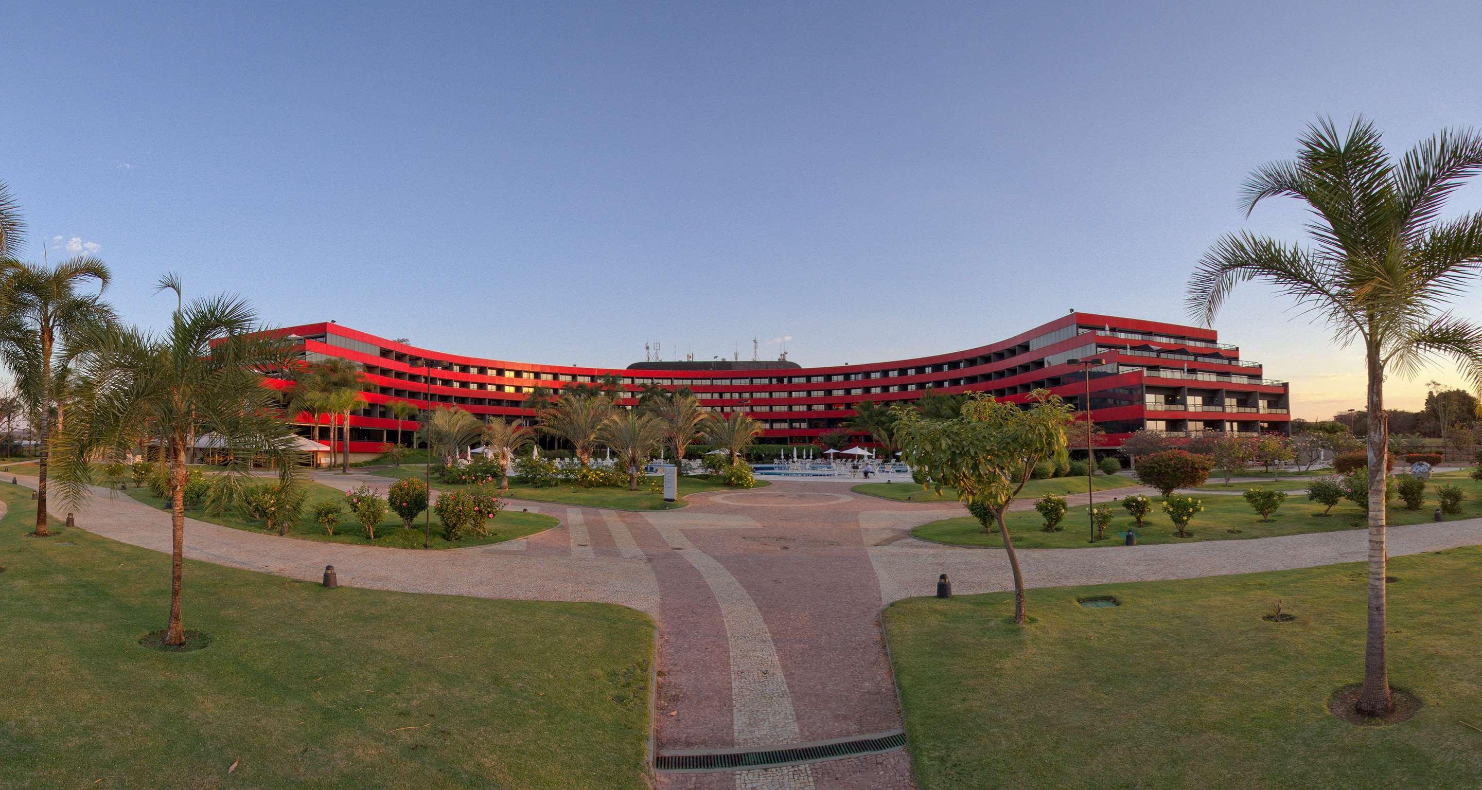 فندق رويال توليب برازيليا ألفورادا المظهر الخارجي الصورة The photo shows a large, curved building with a vibrant red exterior. It appears to be a hotel or resort, surrounded by well-maintained gardens and green spaces. The landscape includes manicured lawns, small trees, and pathways, suggesting a pleasant