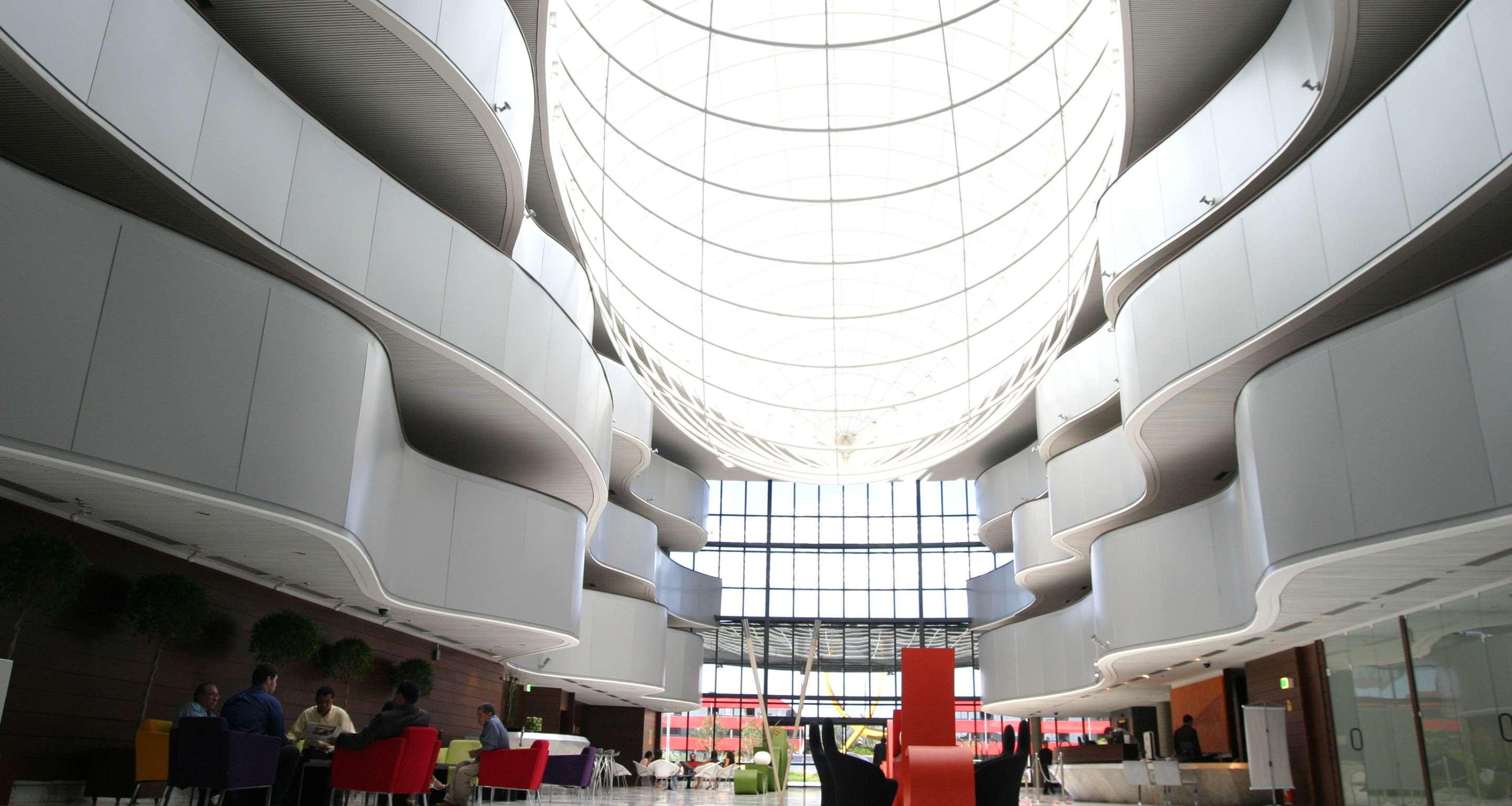 فندق رويال توليب برازيليا ألفورادا المظهر الخارجي الصورة The photo depicts a modern interior space characterized by sleek, curvilinear architecture. The ceiling features a large, dome-like skylight that allows natural light to flood the area. The walls display a minimalist design with smooth, white surface